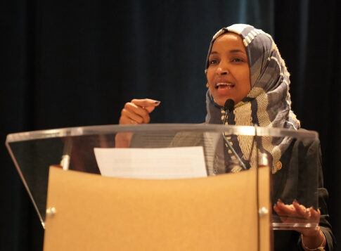A woman in a hijab speaking at a podium during a conference