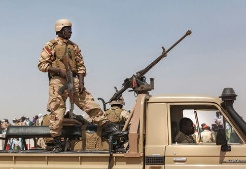 Soldier standing on vehicle with large mounted weapon.