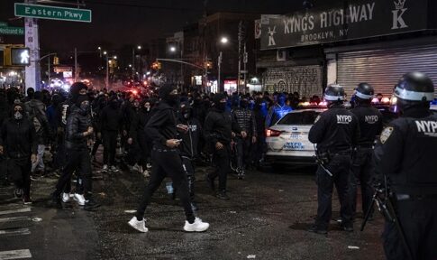 Crowd of people gathered on a street with police officers and vehicles