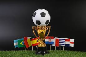 A golden soccer trophy with a black and white ball on top, surrounded by small flags of various countries