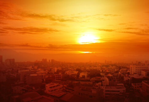 A vibrant sunset over a city skyline with buildings silhouetted against the orange sky