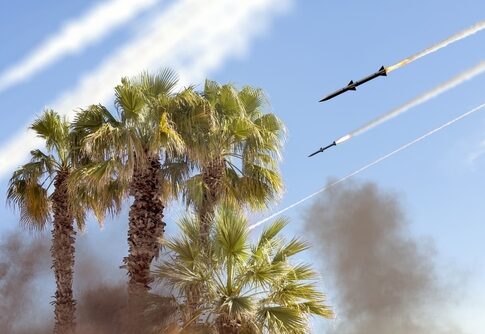 Missiles launching above palm trees with smoke in the background