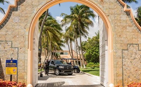 View through an ornate archway leading to a tropical entrance with palm trees and parked cars