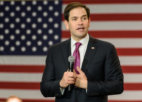 A politician speaking into a microphone in front of an American flag