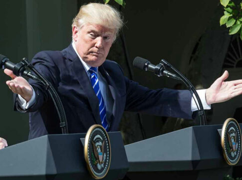 Man speaking at a podium, arms extended outward.