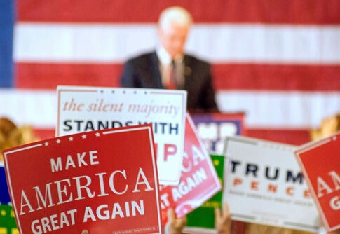 political rally with speaker and campaign signs in front of an American flag